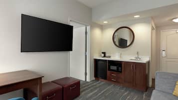 Une chambre d’hôtel équipée d’un téléviseur à écran plat, d’un petit bureau, d’un canapé, d’un four à micro-ondes, d’une machine à café et d’un miroir.