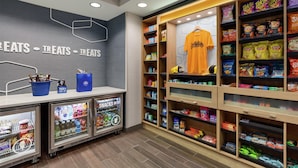 A snack kiosk with various packaged snacks and beverages, a hanging t-shirt, and a refrigerated display case. - Hampton Inn & Suites Pittsburgh/Harmarville (Pittsburgh)