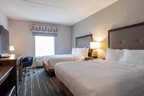 A hotel room with two beds, a desk, a chair, and a large window.