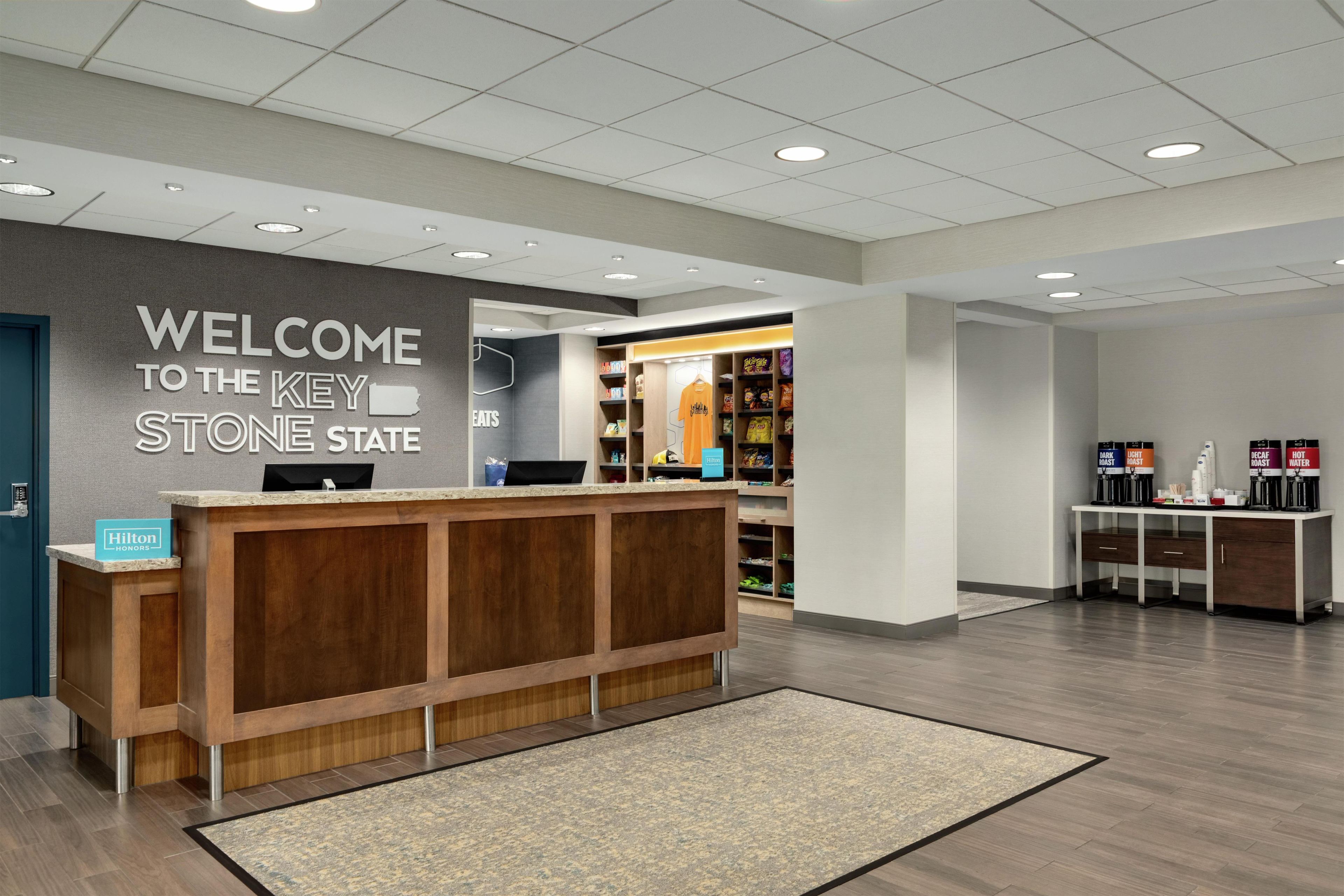 Un hall d'accueil d'hôtel avec un comptoir de réception en bois, une pancarte indiquant « Bienvenue dans l'État de Key Stone » et un kiosque en libre-service.