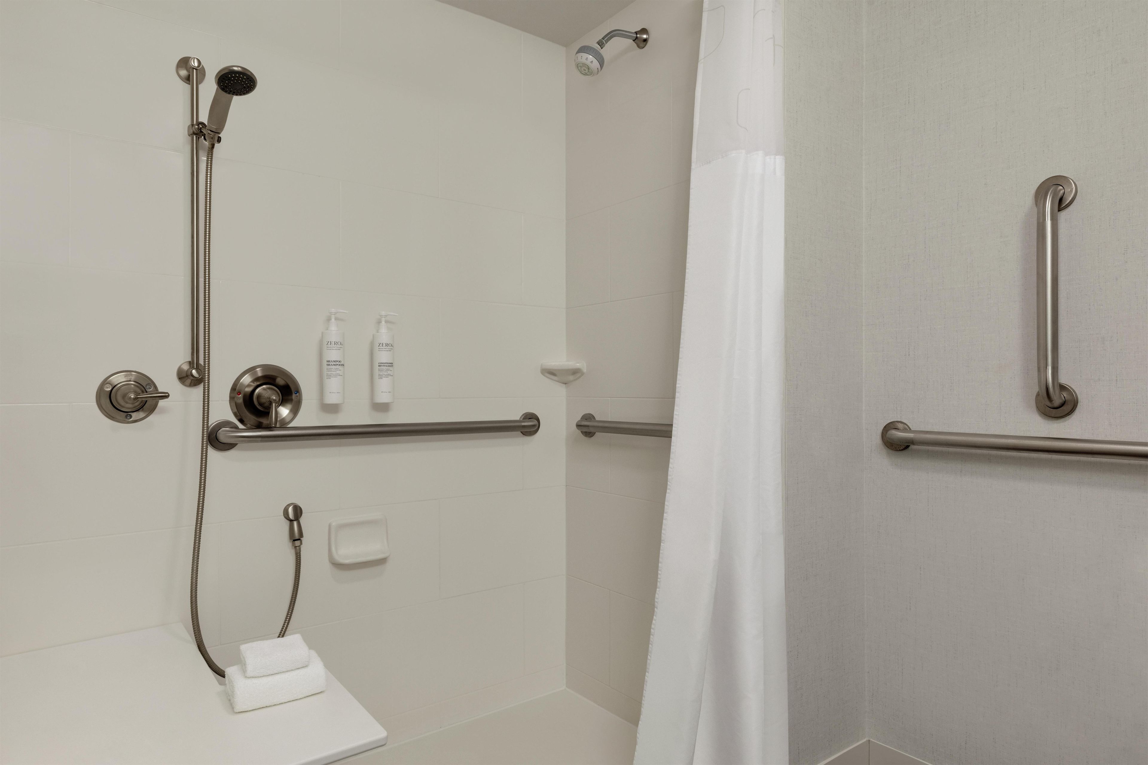 A modern bathroom with a walk-in shower, grab bars, and a towel rack.