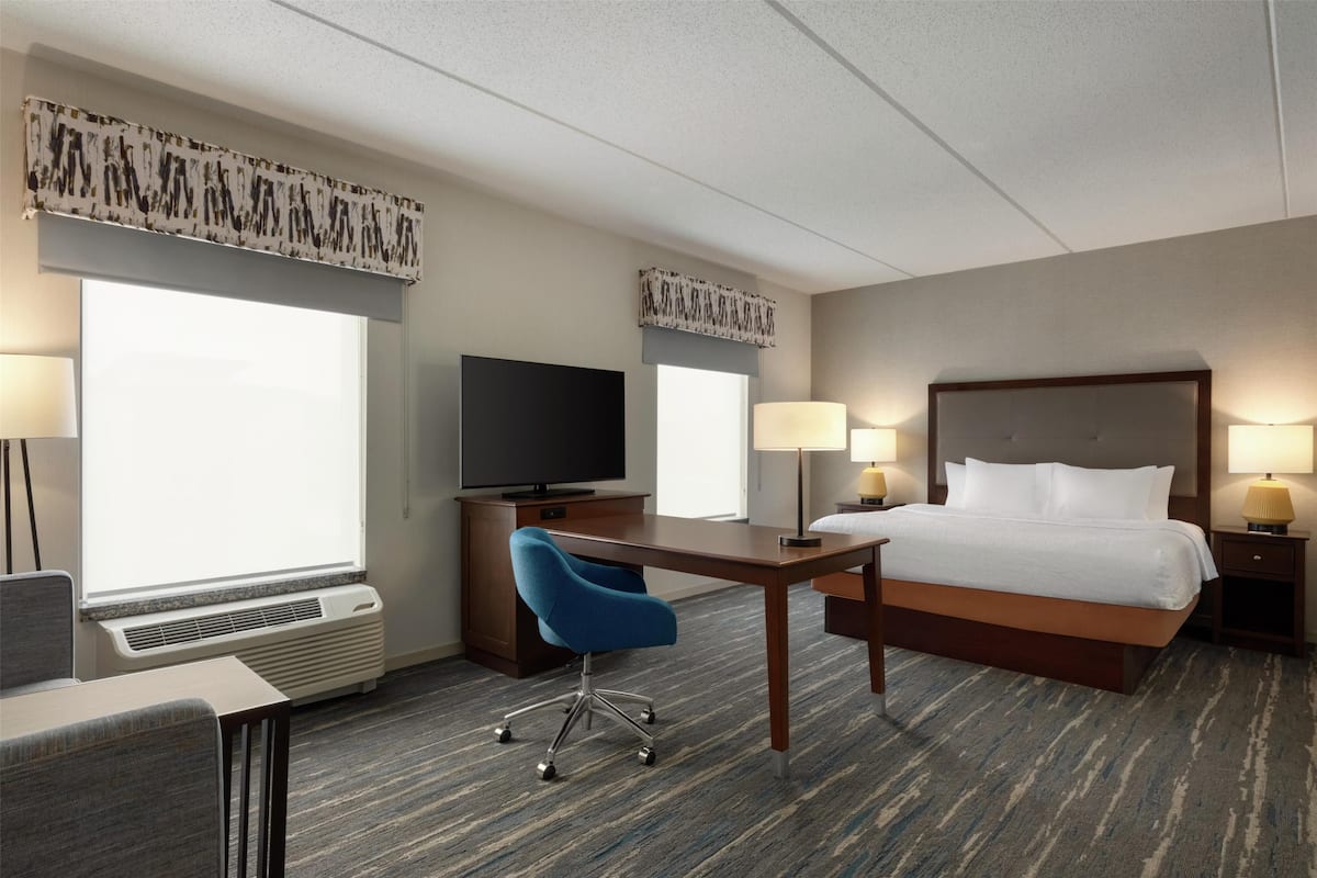 A hotel room with a bed, desk, chair, television, and lamps.