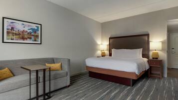 Habitación de hotel con cama, sofá, dos lámparas de noche y un cuadro de una vista urbana en la pared.
