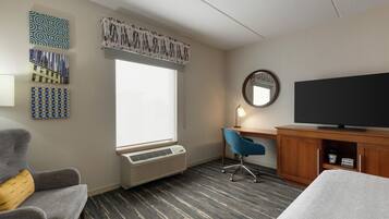 Una habitación de hotel con cama, escritorio con televisor, silla, calentador y obras de arte en las paredes.