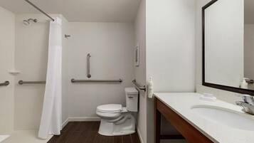 Un baño moderno con inodoro blanco, ducha con cortina blanca, barra de apoyo y lavamanos con espejo.