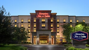 Edificio de Hampton Inn & Suites by Hilton con un cartel llamativo, una entrada bien iluminada y un camino de acceso ajardinado.