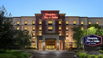 A Hampton Inn & Suites by Hilton building with a prominent sign, a well-lit entrance, and a landscaped driveway.