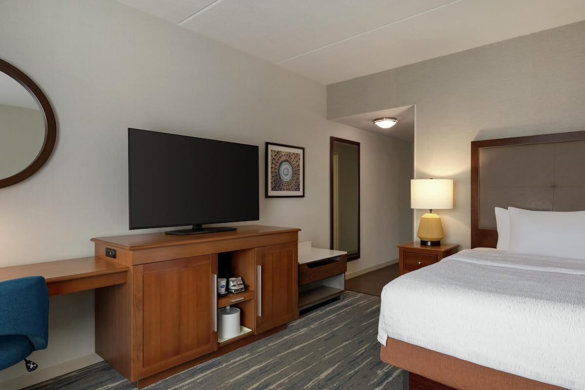 A hotel room with a bed, a TV, a desk, a lamp, and a mirror.