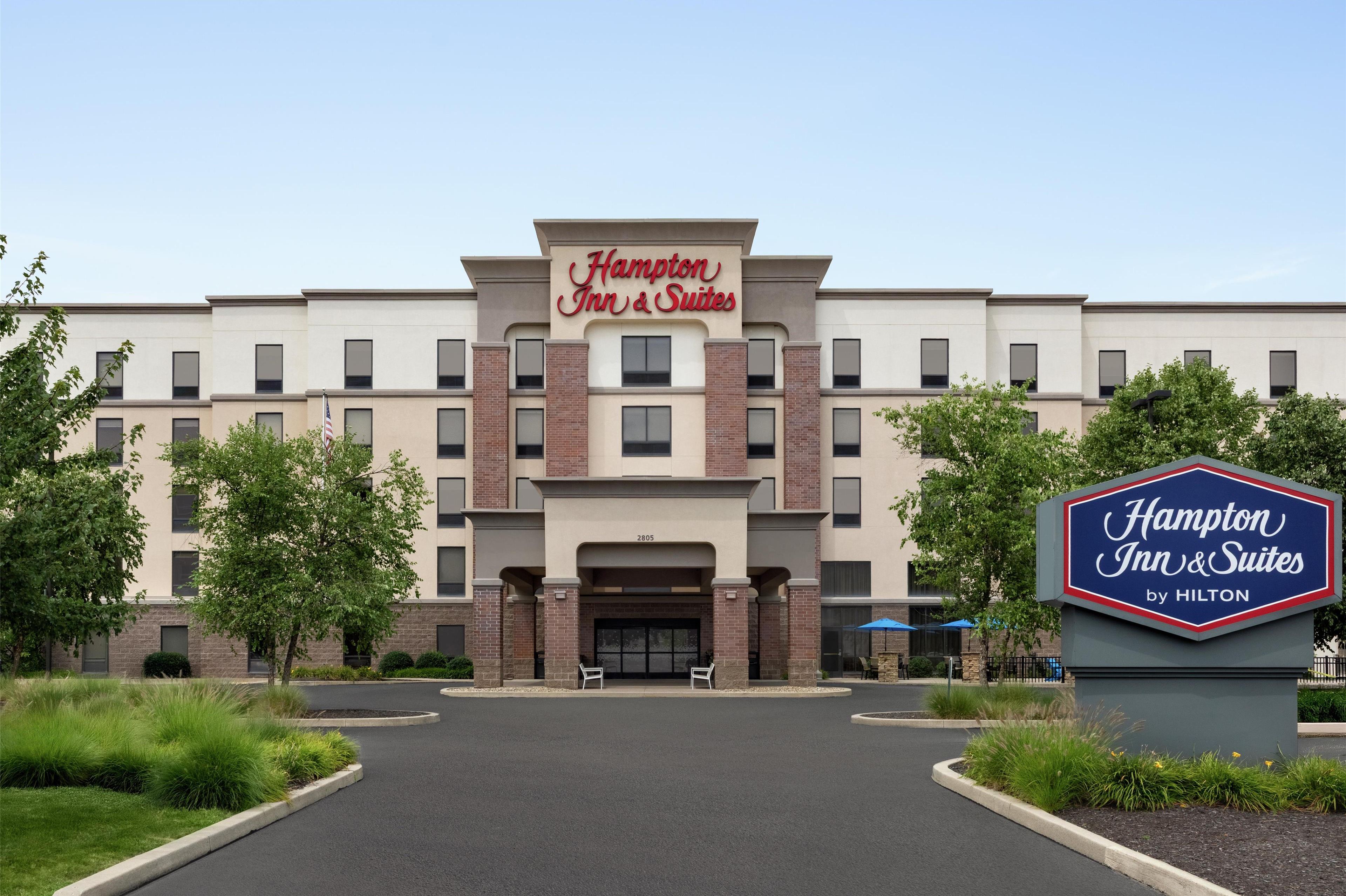 A Hampton Inn & Suites by Hilton building with a modern facade, a central entrance, and a landscaped driveway.