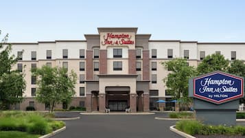 A Hampton Inn & Suites by Hilton building with a modern facade, a central entrance, and a landscaped driveway.