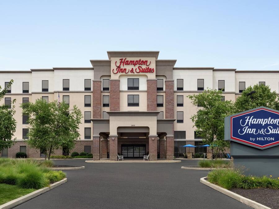A Hampton Inn & Suites by Hilton building with a modern facade, a central entrance, and a landscaped driveway.