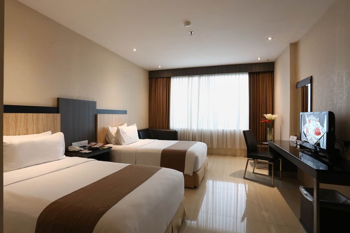 A hotel room with two beds, a desk with a television, and a large window with curtains.