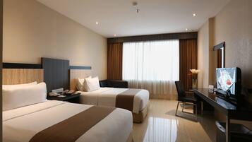 Una habitación de hotel con dos camas, un escritorio con televisor y un amplio ventanal con cortinas.