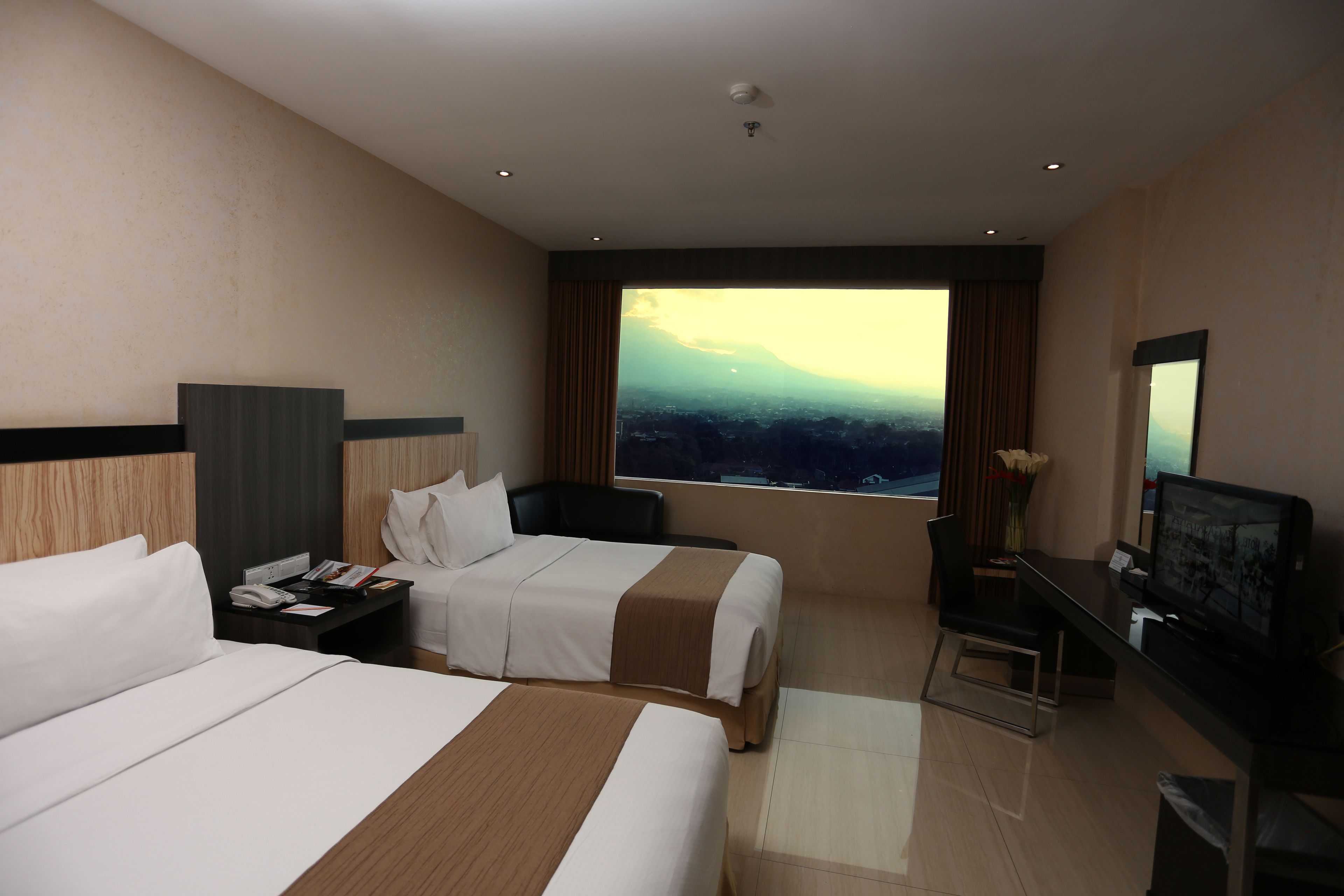 Habitació d'hotel amb dos llits, un escriptori, televisió i una finestra gran amb vista a la ciutat.