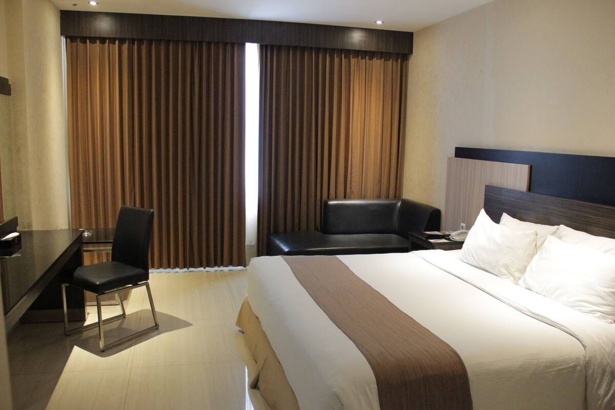 A hotel room with a large bed, a desk, a chair, and a headboard.