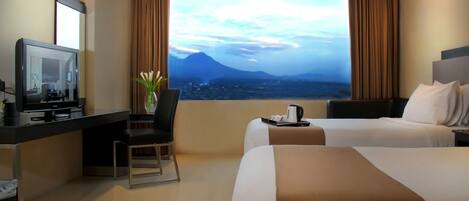 Ein Hotelzimmer mit zwei Betten, einem Schreibtisch mit Fernseher, einem Sessel und Blick auf einen Berg.