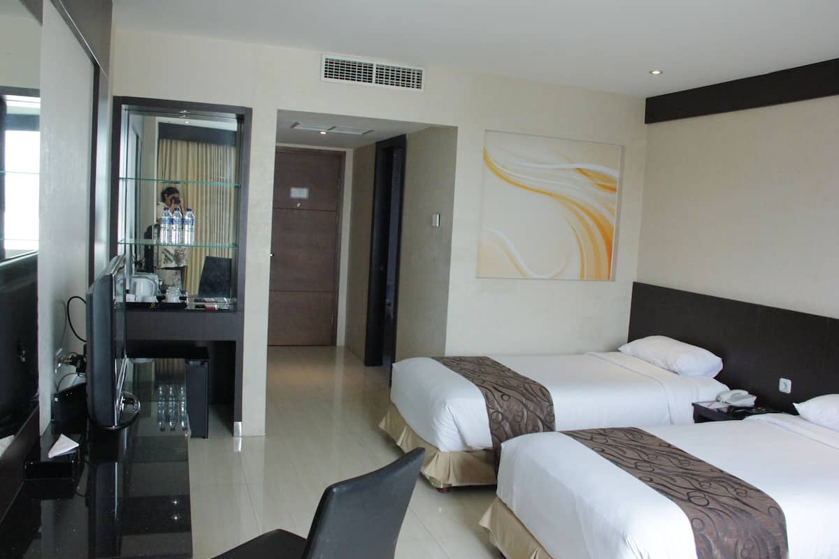 A hotel room with two beds, a desk with a chair, a mirror, and a painting on the wall.