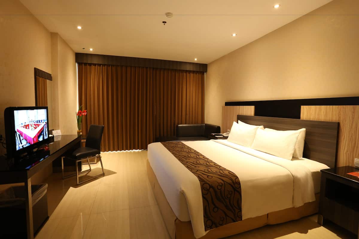 A hotel room with a large bed, a desk with a television, a chair, and a nightstand.
