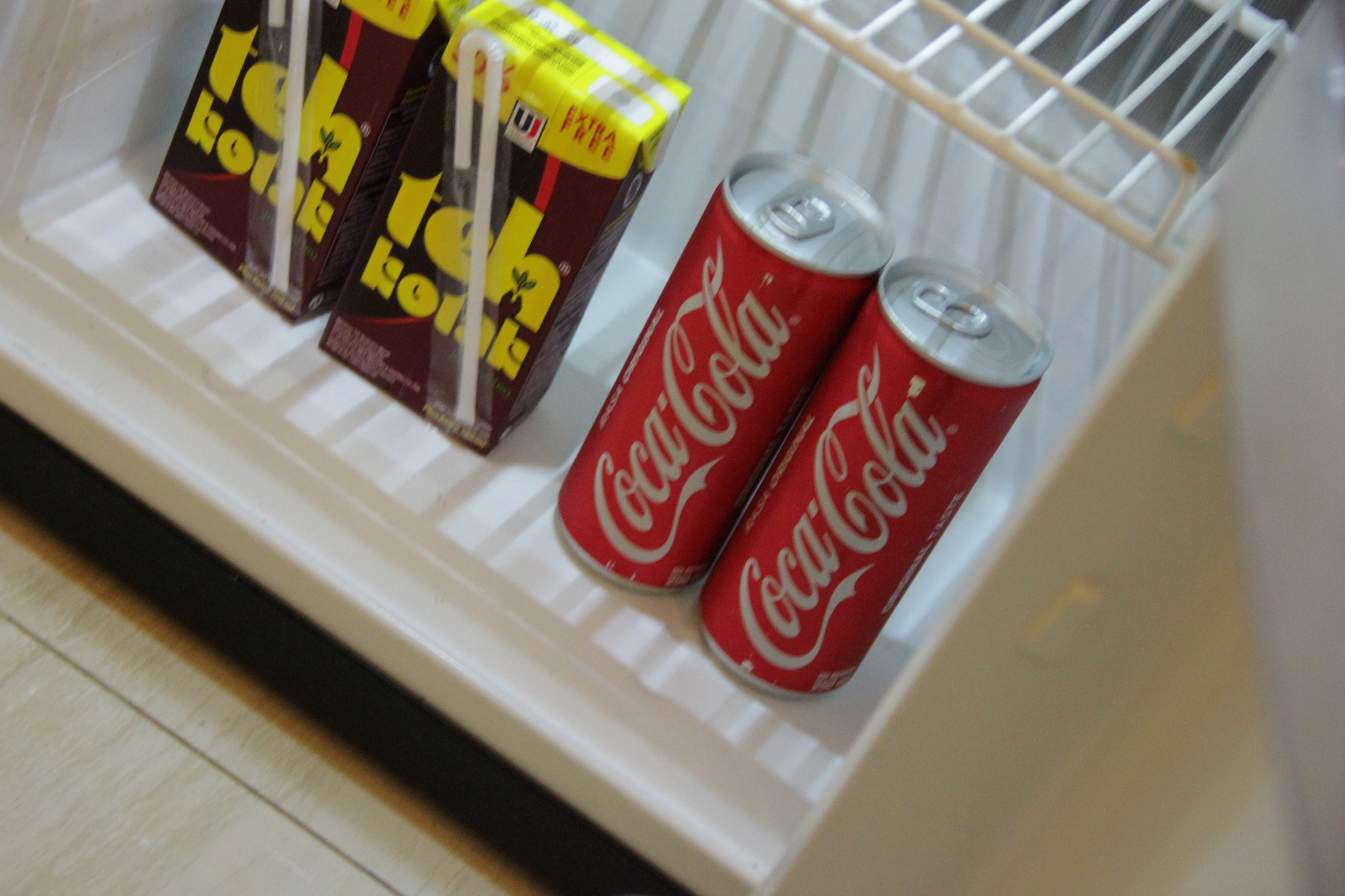 A refrigerator with three cartons of juice and two cans of Coca-Cola.