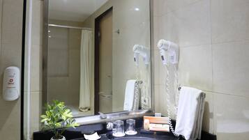 A bathroom with a large mirror, a sink, a hairdryer, a towel, and a trash bin.