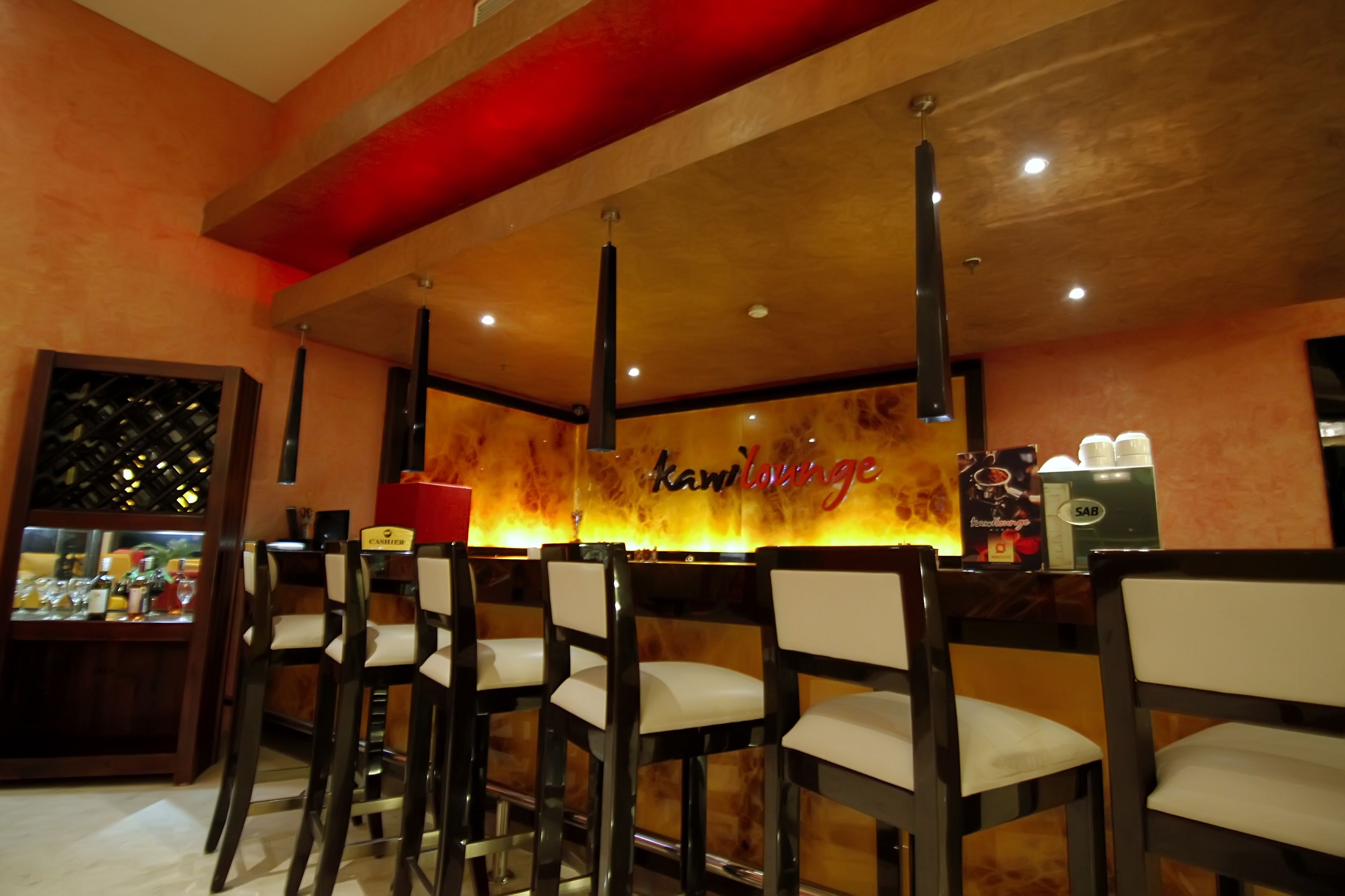 Un espace bar avec des chaises en bois et un comptoir où est affiché le logo de « Kawilounge ».