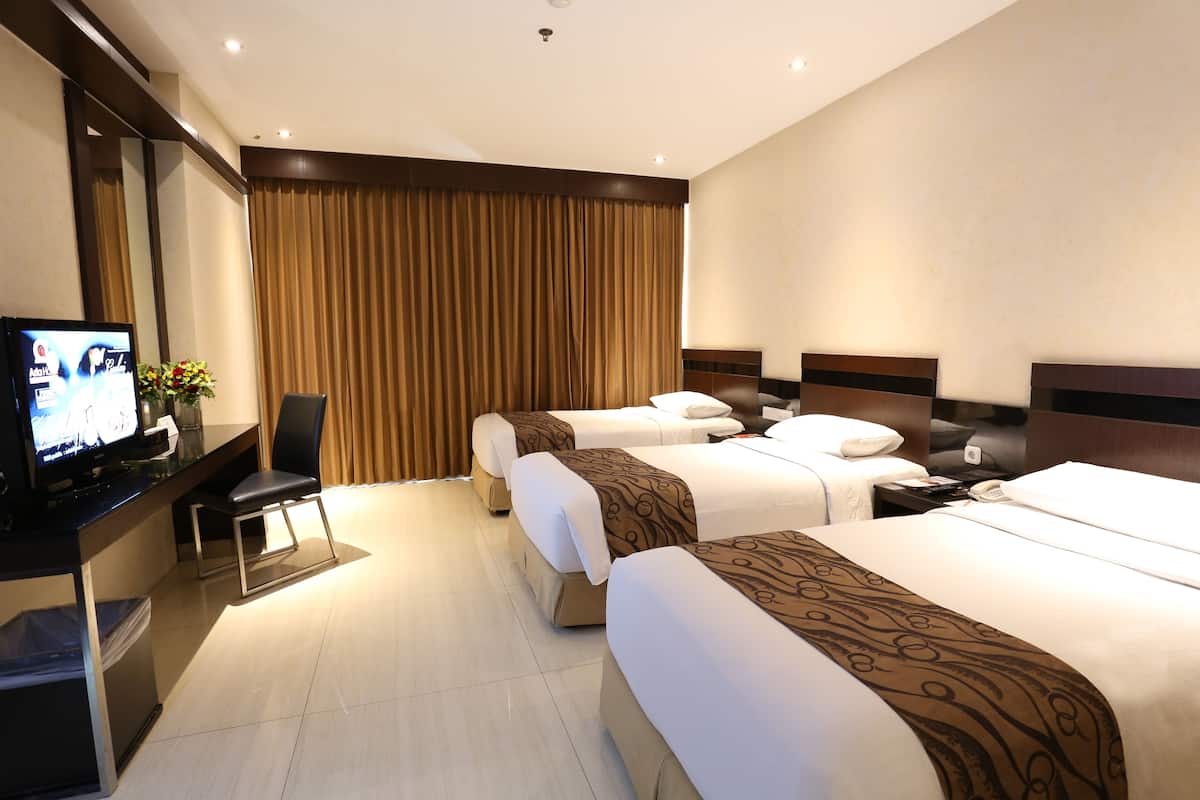 A hotel room with three beds, a TV, a desk with a computer, and a chair.