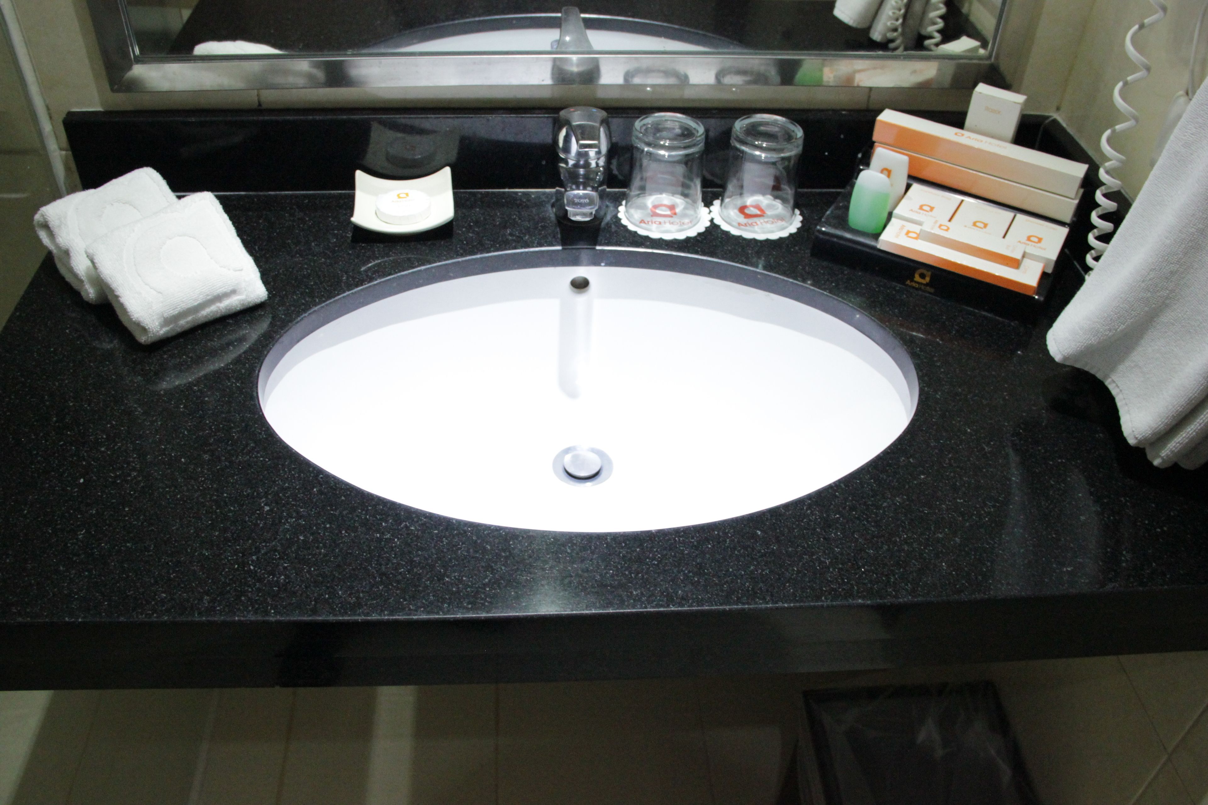 A hotel bathroom with a black countertop, a white sink, and toiletries including a soap dispenser, two glass bottles, and a towel.