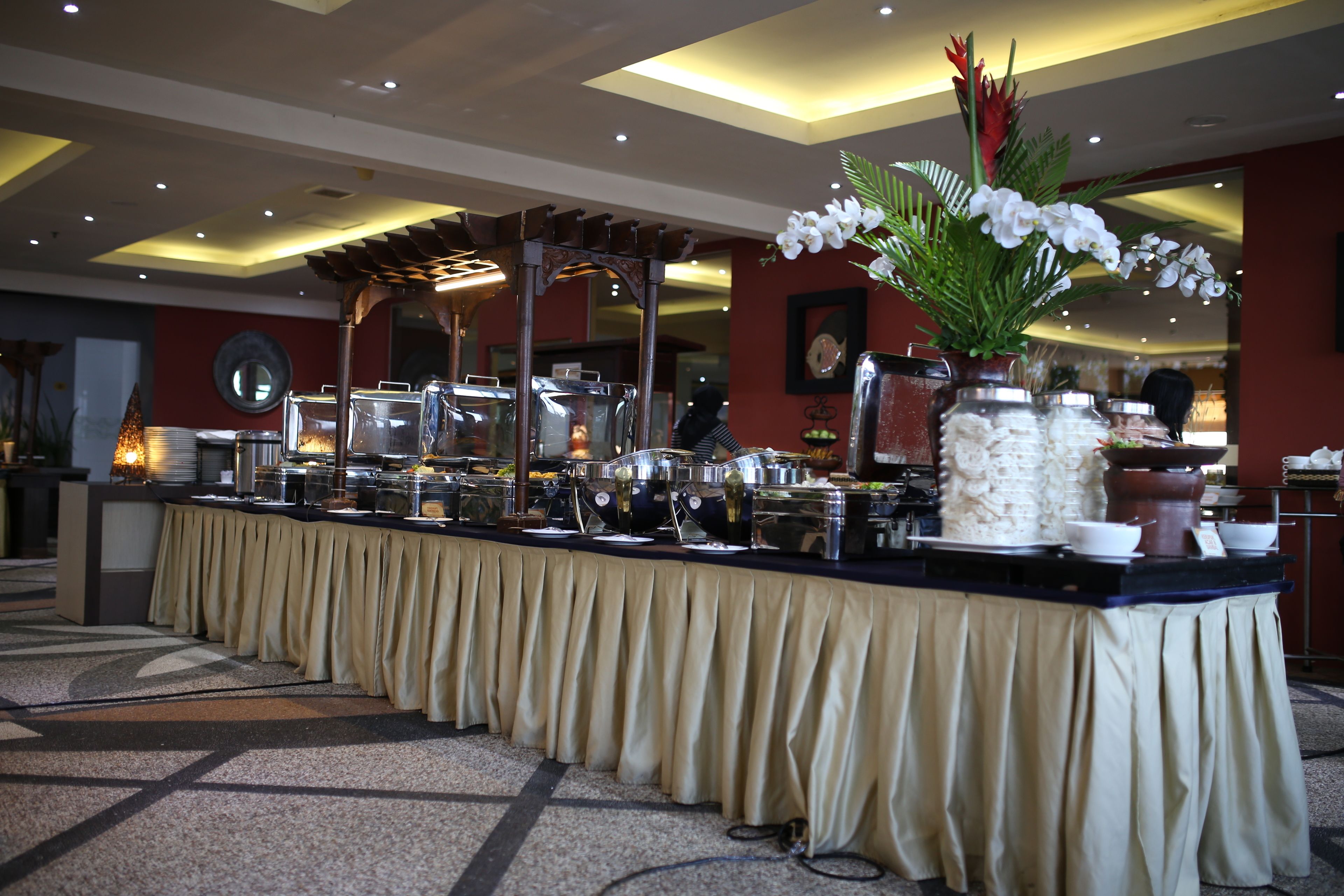 A buffet setup with a long counter, various food containers, and a decorative plant.