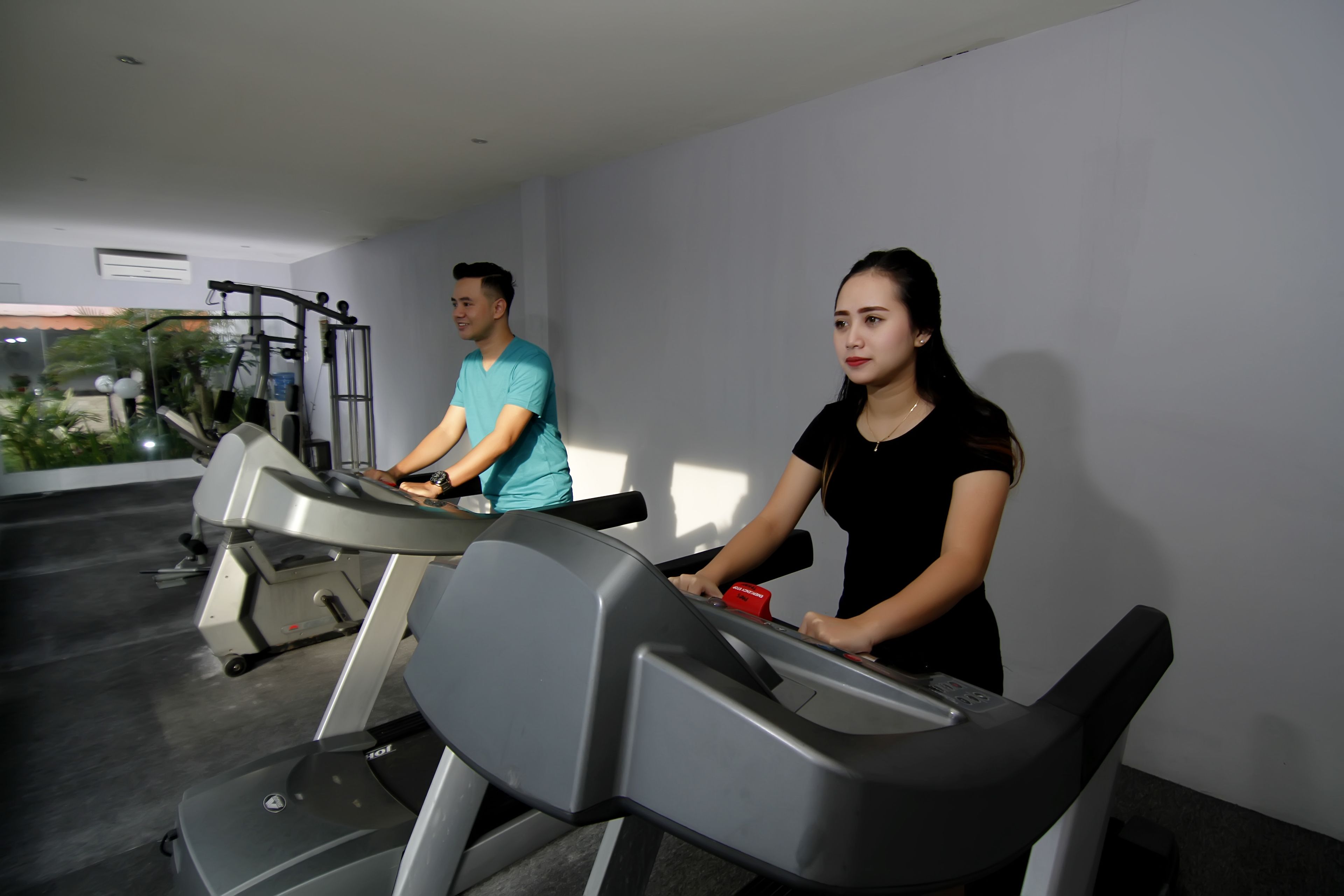 Dos personas usando cintas de correr en un gimnasio con vistas a zonas verdes.