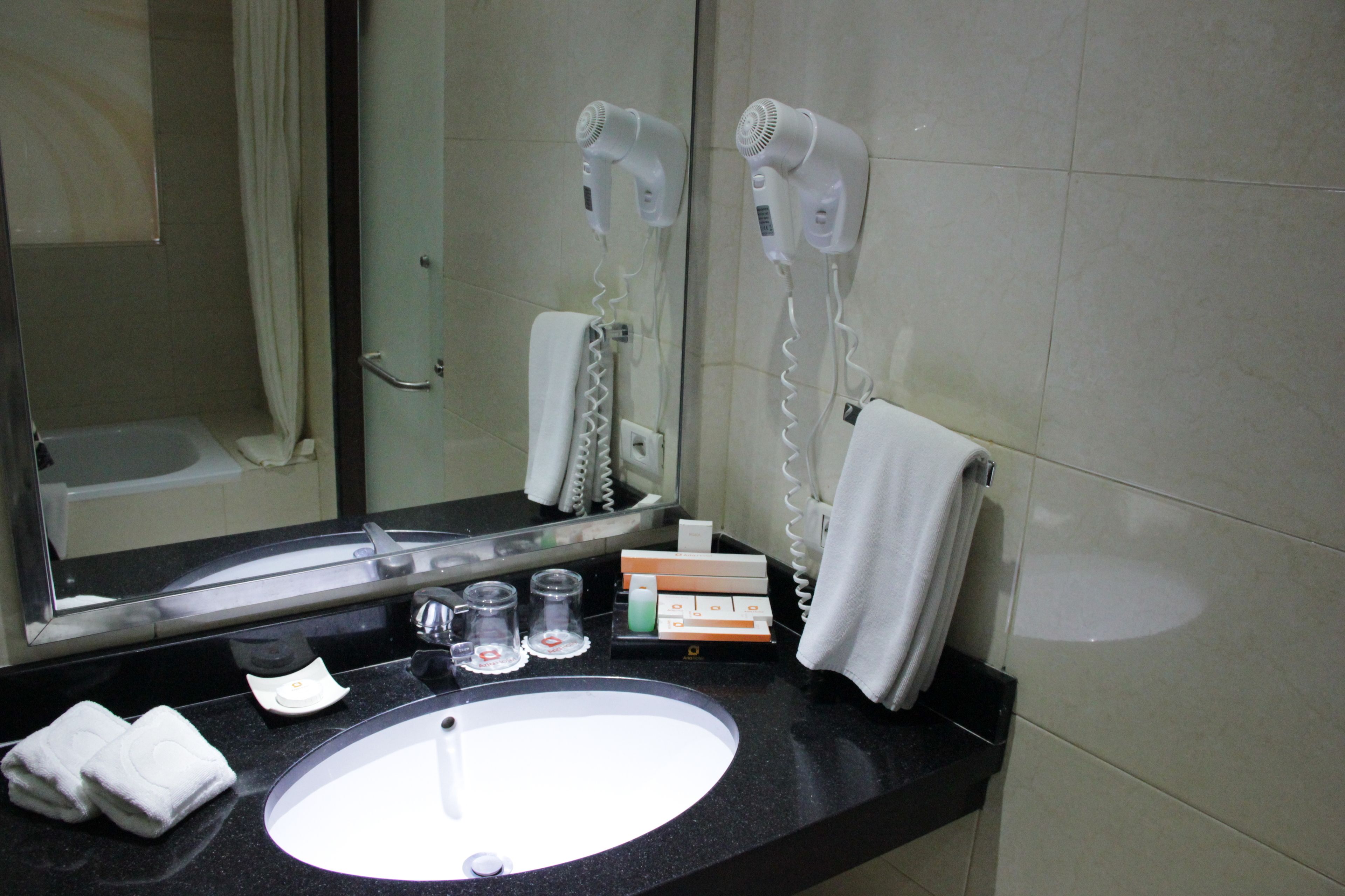 A bathroom with a sink, two hair dryers, a mirror, a towel, and toiletries.
