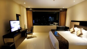 Una habitación de hotel moderna con una cama grande, un escritorio con una computadora portátil, un televisor y vistas a la ciudad de noche.