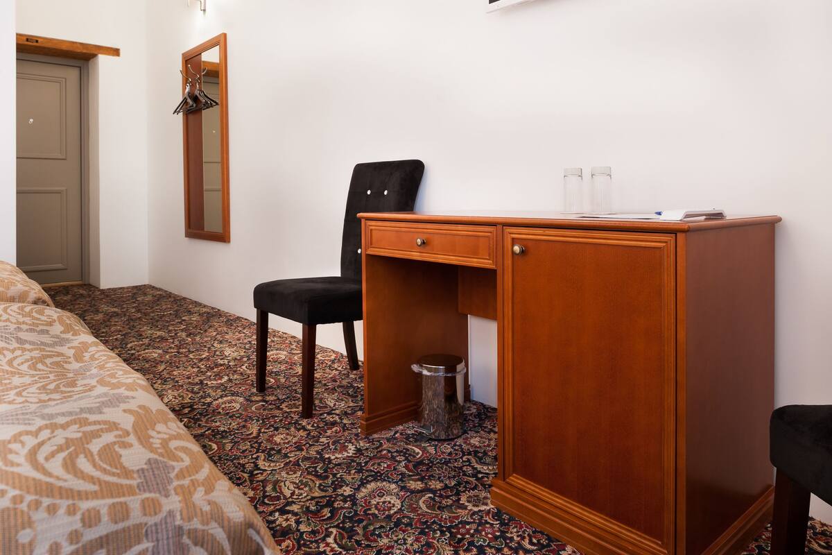 Ein Hotelzimmer mit Bett, Schreibtisch mit Stuhl, Spiegel und Mülleimer.