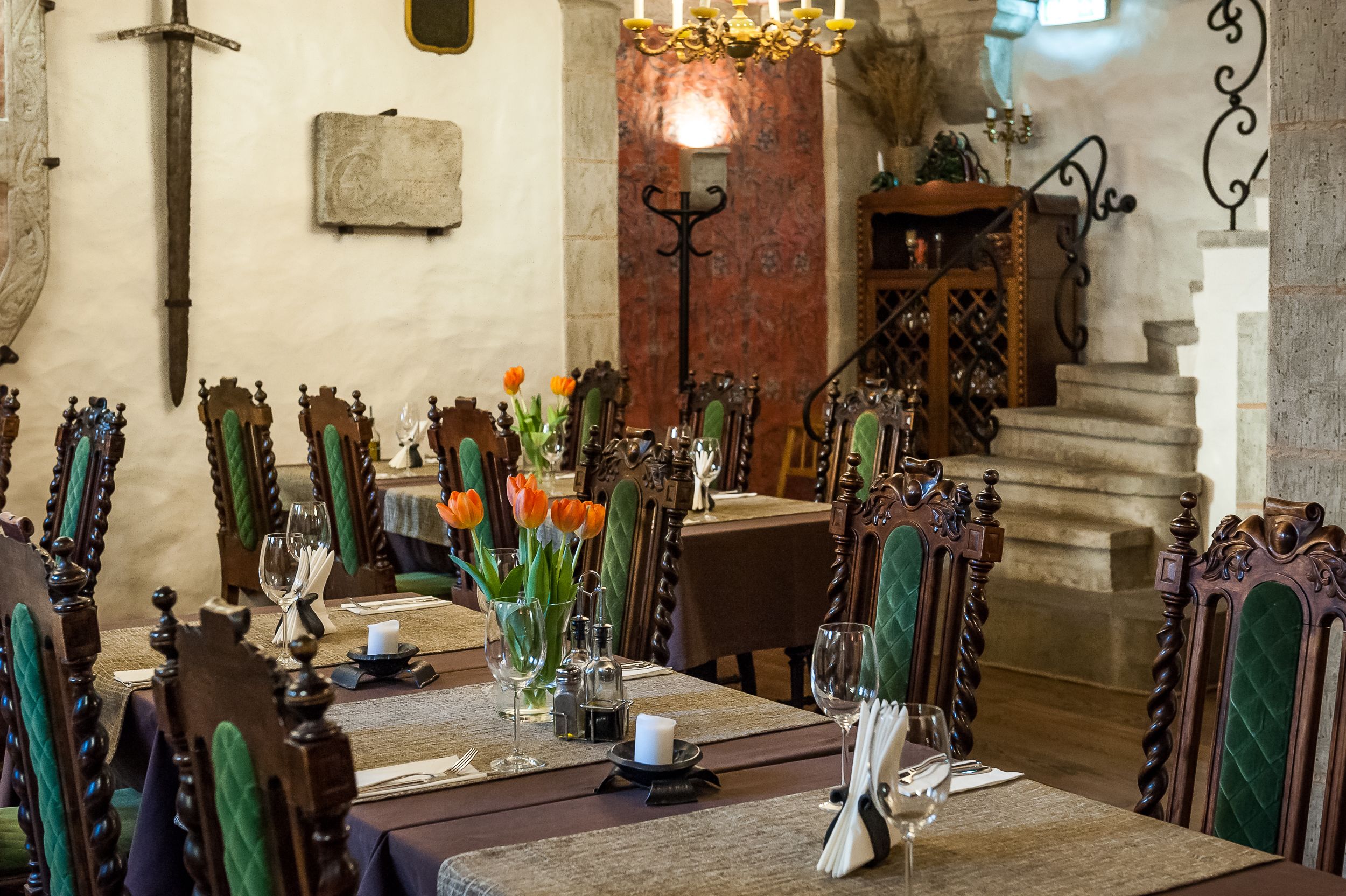 A dining area with wooden tables and chairs, a chandelier, and a stone staircase.