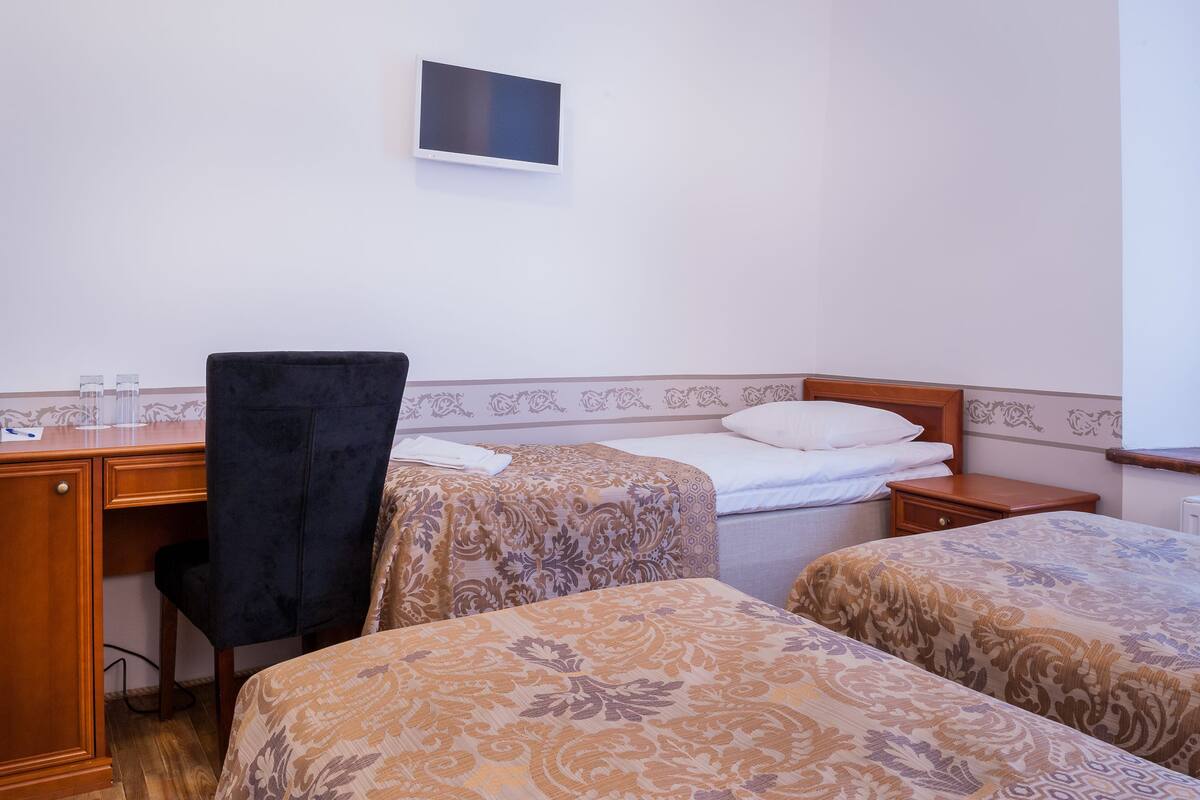 Ein Hotelzimmer mit zwei Betten, einem Schreibtisch, einem Stuhl und einem an der Wand befestigten Fernseher.