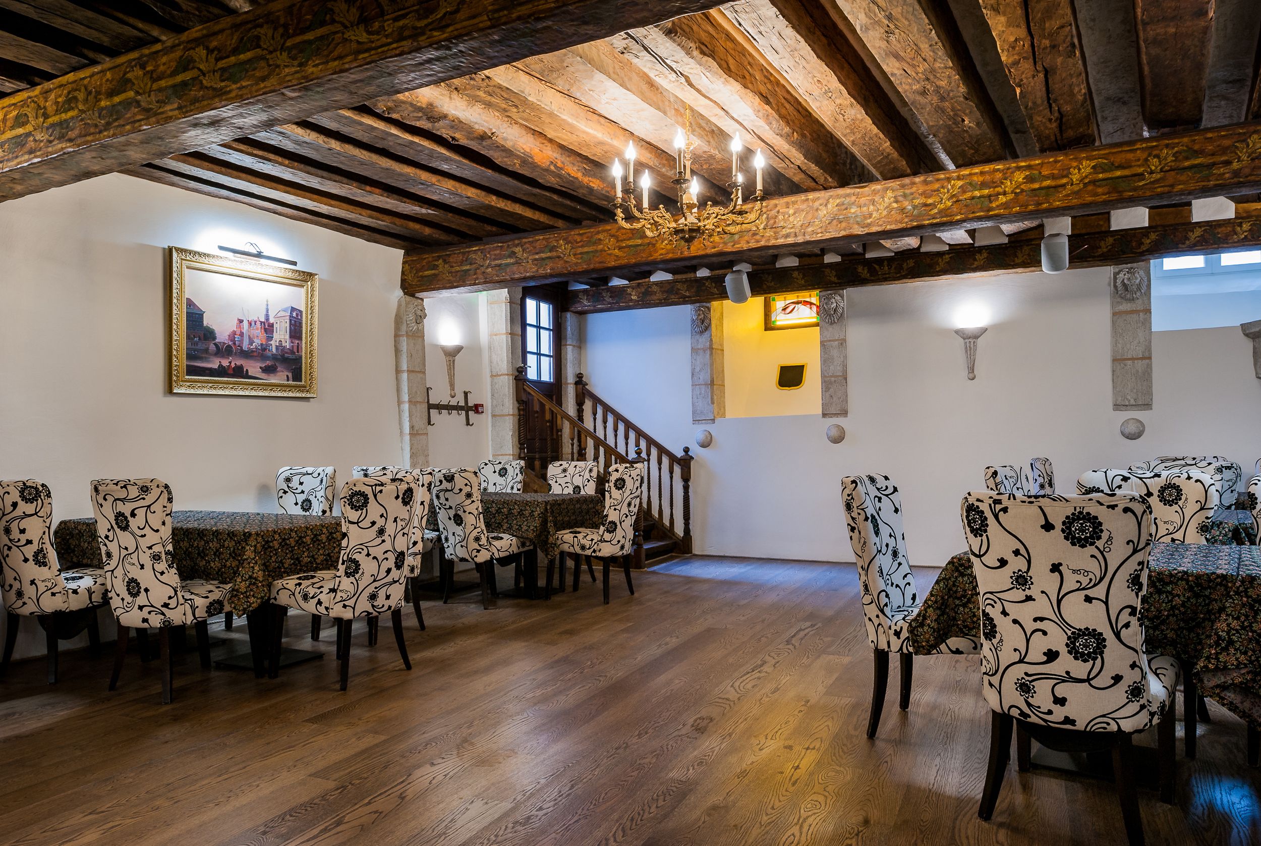 A dining area with wooden beams, patterned chairs, and a chandelier.