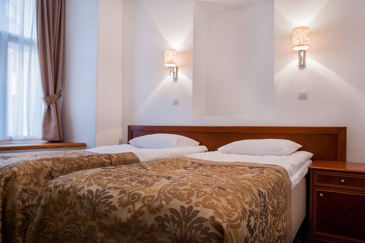 Ein Hotelzimmer mit zwei Betten, einem hölzernen Kopfteil, einem Nachttisch und Wandlampen.
