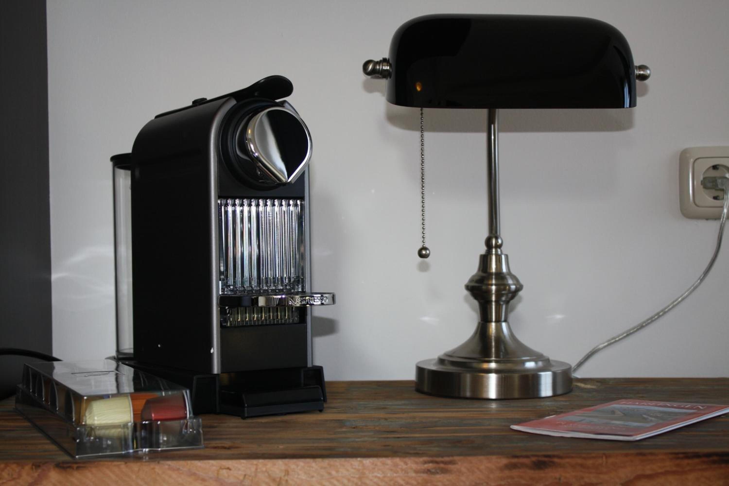 Une machine à café, une lampe et un magazine sur une table en bois.