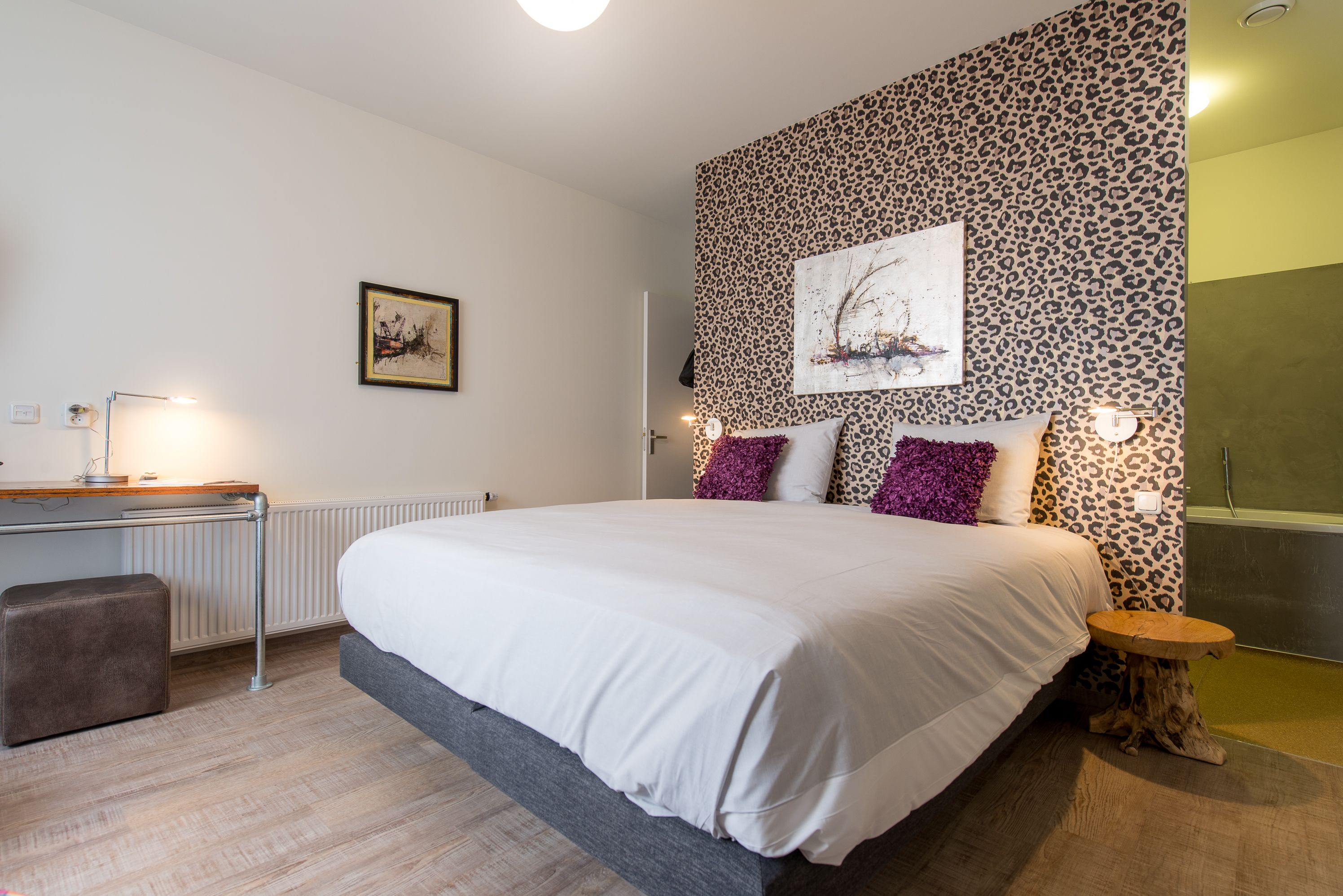 A bedroom with a large bed, a desk with a lamp, a radiator, and a leopard print wall.