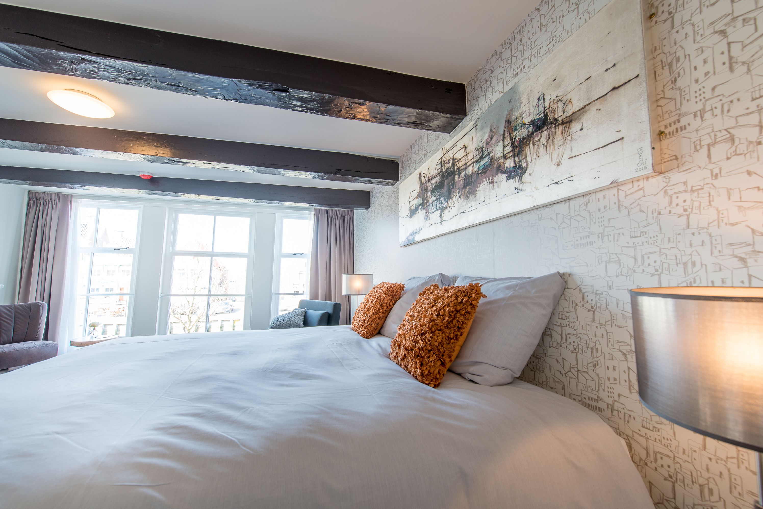 Ett hotellrum med en stor säng, utsikt över staden genom fönstret och en modern takdesign.