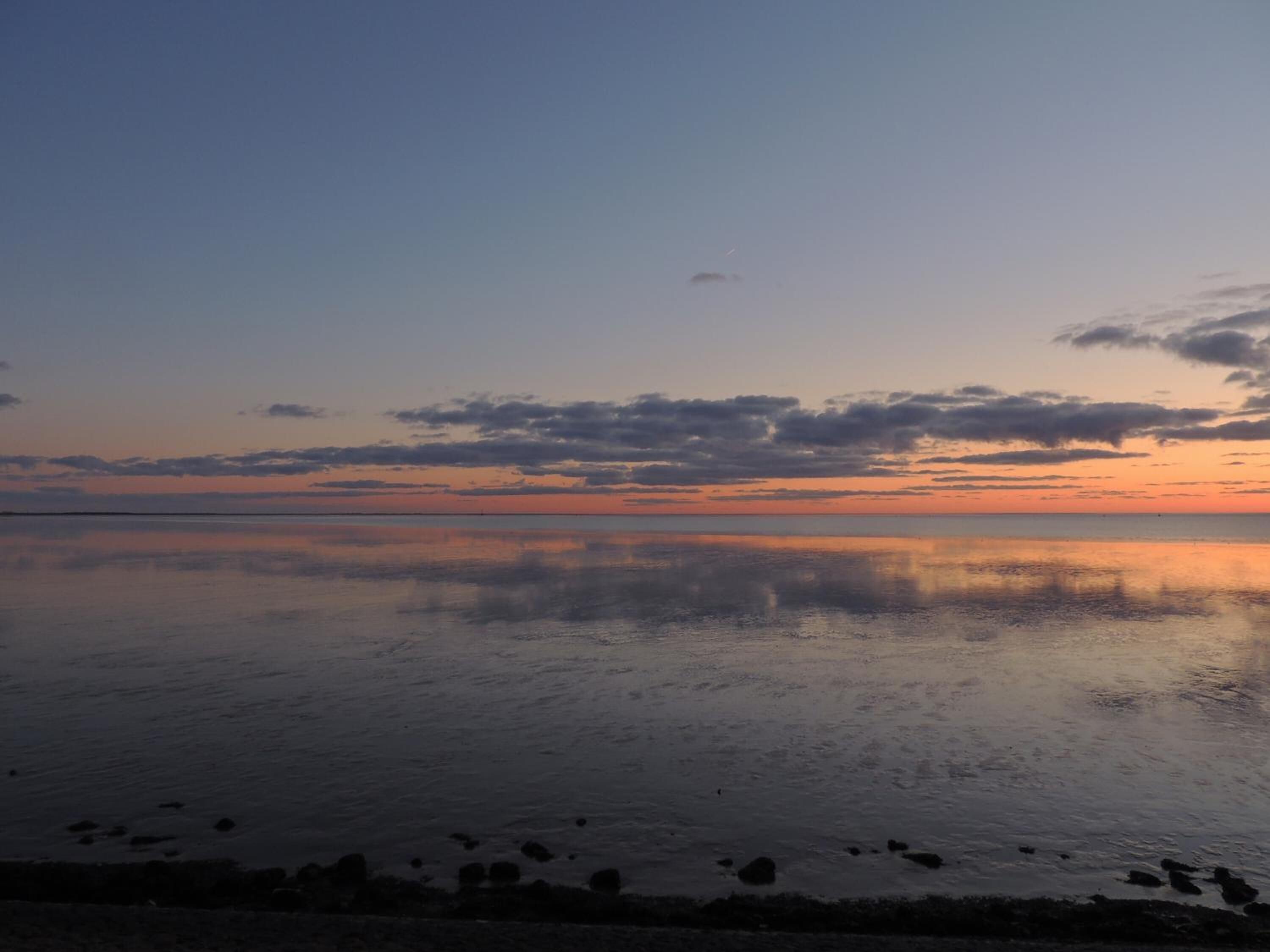 En stilla vattenyta som speglar himlen under solnedgången.