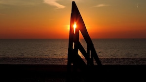 Un atardecer sobre el océano con la silueta de una estructura en primer plano.
