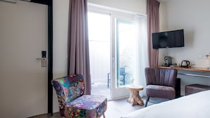 Habitación de hotel con cama, escritorio con televisor, una silla y vista al exterior.