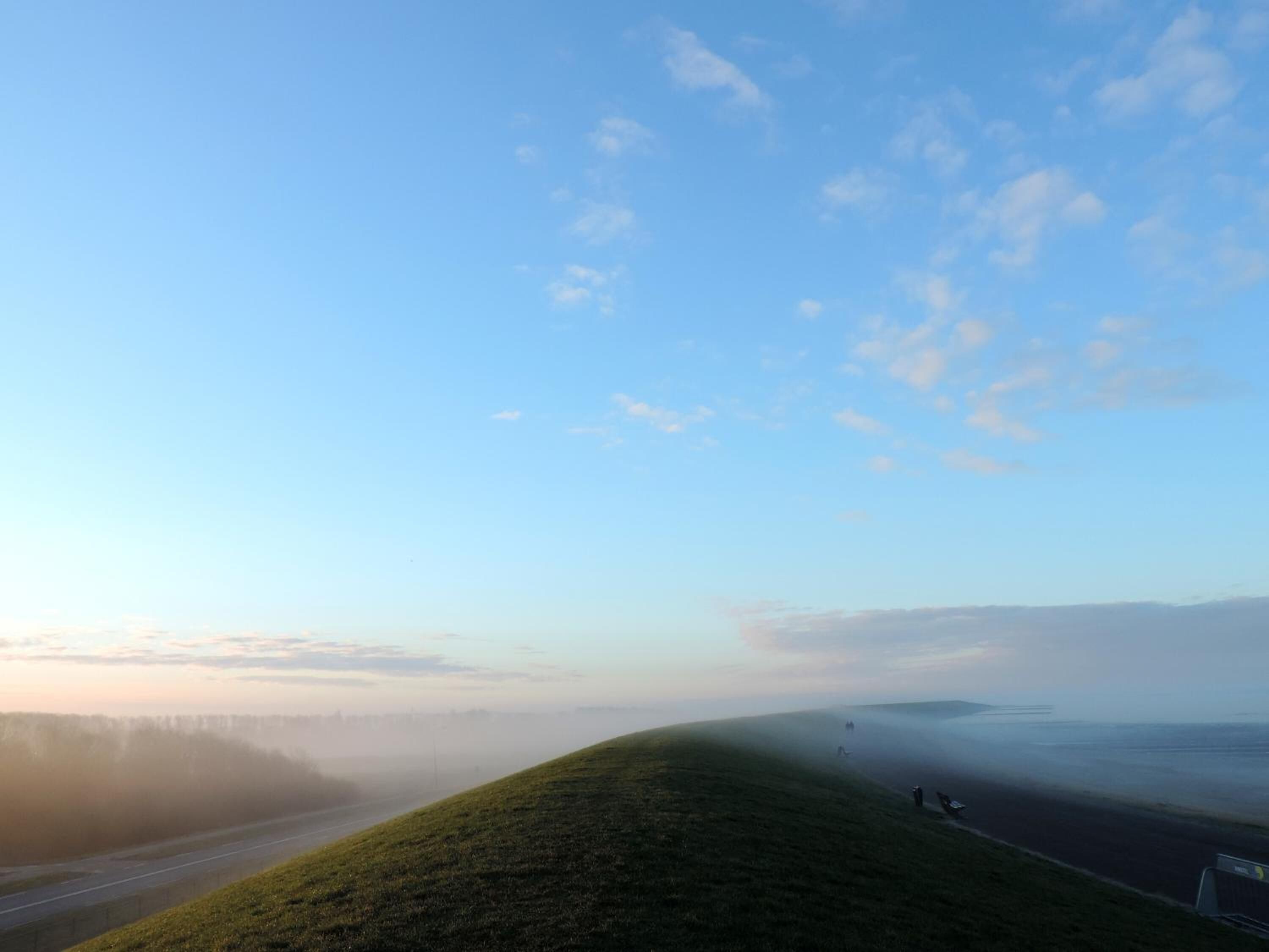A road curving through a grassy landscape with a clear sky and distant mountains.