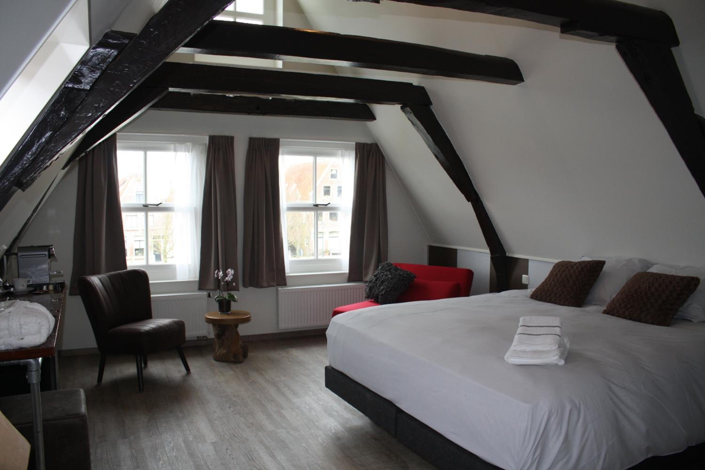 Ein Schlafzimmer mit schräg verlaufender Decke, einem Bett mit weißen Leinen, einem roten Sessel und einem Schreibtisch mit einem Computer.