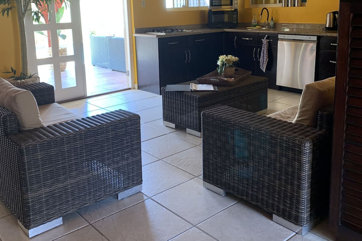 A bright kitchen with a microwave, stove, and sink. There are wicker chairs and a small table in the living area.