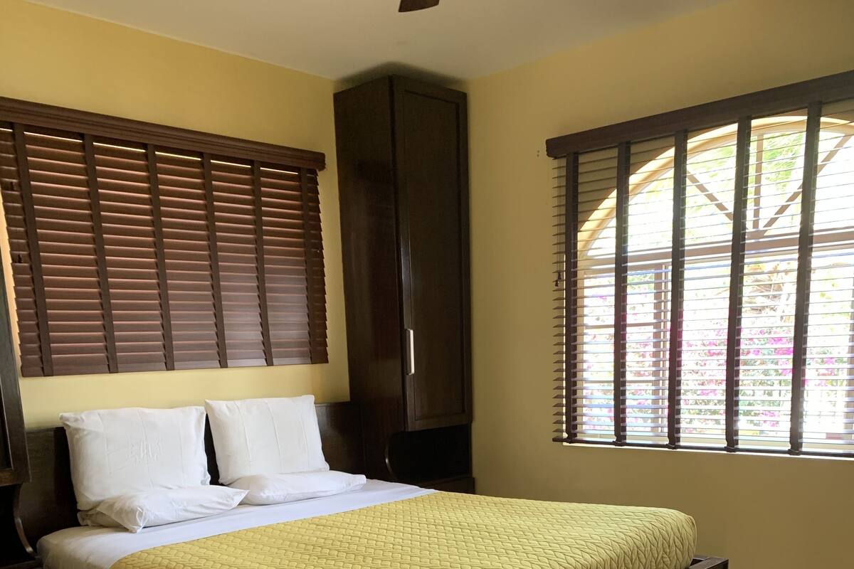 A bedroom with a bed, wooden headboard, wardrobe, and a window with blinds.
