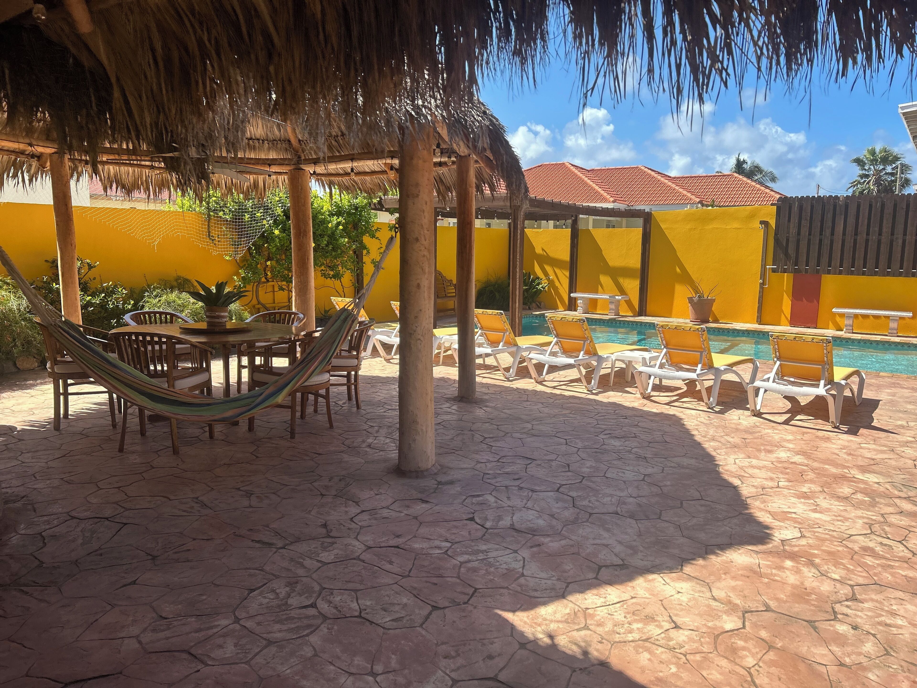 Un patio con piscina, sillas de descanso, una mesa y una hamaca.