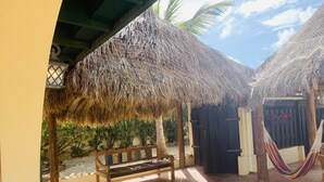 Un espacio al aire libre techado con un banco de madera, una hamaca y estructuras de techo de paja.