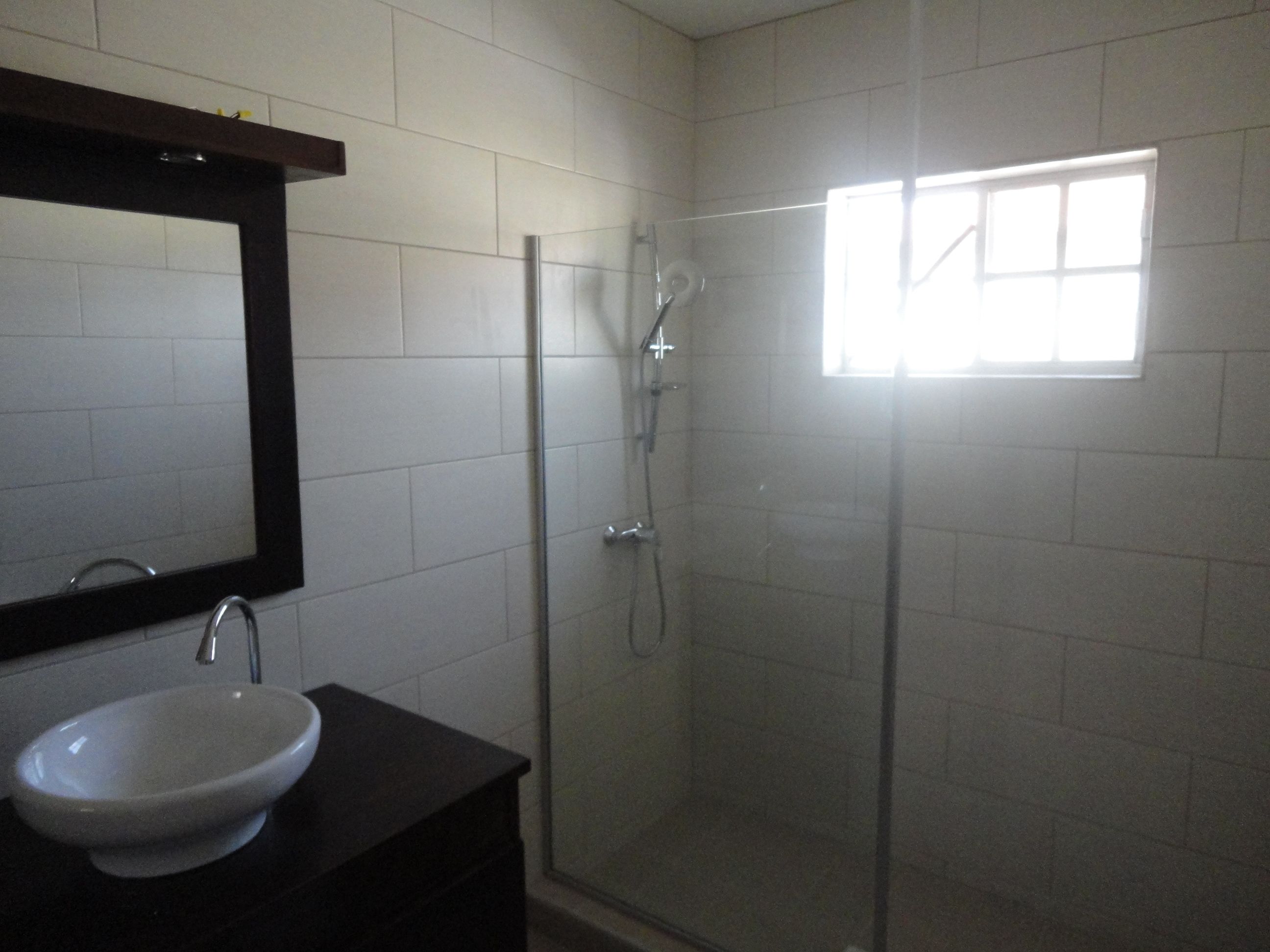 A bathroom with a white sink, a dark vanity, a mirror, and a glass-enclosed shower.
