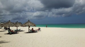 Una playa con sombrillas de techo de paja y sillas reclinables, cielo despejado y aguas turquesas tranquilas.